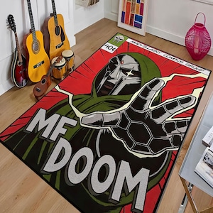 以下が含まれることがあります： MF DOOMのコミック風イラストが描かれた長方形のラグ。緑色のフード付きの人物がメタリックマスクと手を伸ばし、赤と黒の背景に配置されています。「MF DOOM」の文字が大きく表示されています。