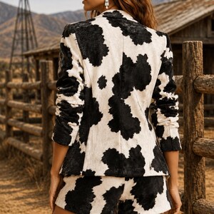May include: A blazer and shorts set featuring a black and white cow print pattern. The blazer has long sleeves with gathered detailing and a notched collar. The matching shorts are cut to a mid-thigh length, completing the coordinated two-piece outfit.