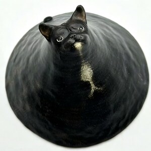 May include: A black ceramic sculpture of a dog with a round body and a small head. The dog has a white patch on its chest and is looking upwards. The sculpture has a glossy finish and is set against a white background.