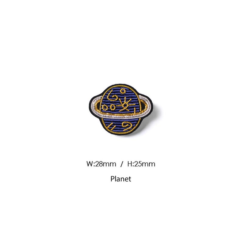May include: A circular embroidered patch featuring a dark blue planet with gold stitched celestial symbols and a silver ring. The patch measures 28mm in width and 25mm in height, with the text Planet printed below the design.