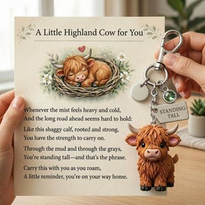 May include: A keyring with a brown Highland cow charm, a silver clasp, and a tag that reads "STANDING TALL". The accompanying card says "A Little Highland Cow for You" and features a poem and an illustration of a sleeping calf.