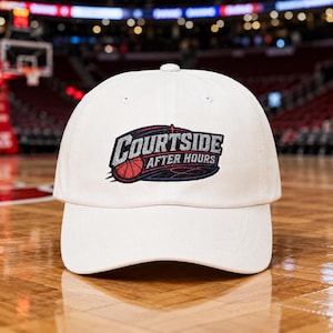 May include: A white baseball cap featuring an embroidered logo on the front. The logo displays the text COURTSIDE AFTER HOURS in silver and black lettering, accompanied by a red basketball graphic and a dark blue oval background element.