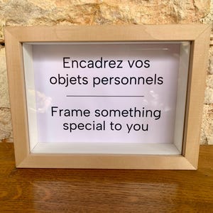 Peut inclure: Un cadre en bois rectangulaire avec un intérieur blanc. Le cadre contient un papier blanc avec le texte "Encadrez vos objets personnels" au-dessus de la ligne et "Frame something special to you" en dessous.