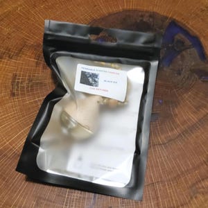 May include: A black plastic bag containing a car air freshener. The label reads "Desirable Scented Candles" and "Black Ice Car Diffuser". The air freshener is visible through the clear plastic, with a wooden base and gold-colored accents.