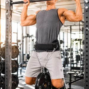 May include: A weightlifting belt with a chain and weight plates. The black belt is worn around the waist and has a chain attached to it. The chain is connected to two black weight plates, each labeled with 10 kg.