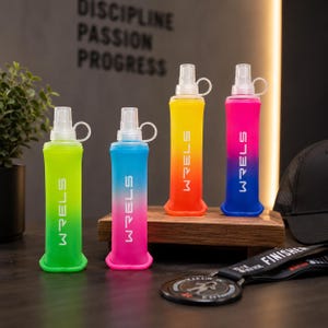 May include: Four colorful, collapsible water bottles with white tops and the word "WRELS" printed vertically. The bottles are arranged on a wooden stand, with a black hat and a medal in the foreground. The bottles are green, blue, yellow, and pink.