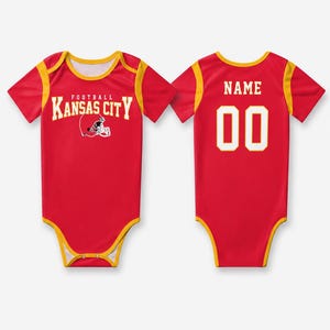 May include: A red and yellow short-sleeve bodysuit featuring the text Kansas City Football with a helmet graphic on the front. The back displays the word NAME above the number 00 in white lettering with a yellow outline on a red background.
