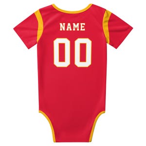 May include: A red short-sleeved bodysuit with yellow trim on the neckline, sleeves, and leg openings. The back features the word NAME in white block letters above the large white numbers 00, which are outlined in a thin yellow border.