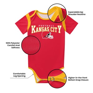 May include: A red and yellow baby bodysuit featuring the text KANSAS CITY FOOTBALL and a white football helmet graphic. It includes an expandable lap shoulder neckline, 100% polyester fabric, comfortable leg openings, and a higher-in-the-front bottom snap closure.
