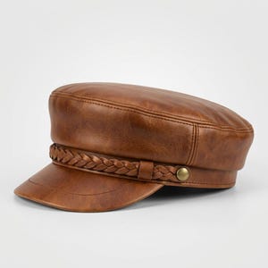 A brown faux leather fiddler news boy cap featuring a structured flat top and a short, stiff peak. A braided faux leather band wraps around the base of the crown, secured on each side by a small, round, metallic brass-coloured button detail.