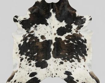 Puede incluir: Alfombra de piel de vaca con un patrón natural de manchas negras y marrones sobre un fondo blanco. La alfombra tiene una forma irregular, típica de la piel de vaca, y es adecuada para la decoración del hogar. La piel es suave y tiene una textura natural.