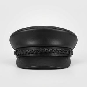 A black leather fiddler newsboy boy cap featuring a smooth rounded crown and a short, stiff brim. A decorative braided leather band wraps horizontally around the base of the crown, secured by small leather loops on each side of the hat.