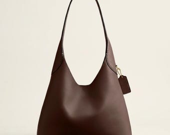 Peut inclure: Un sac à bandoulière en cuir marron foncé avec une seule sangle. Le sac a une forme triangulaire avec une large ouverture et une petite étiquette attachée sur le côté. Le sac est en cuir lisse et a un design simple et élégant.