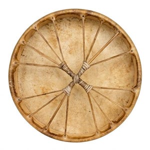 May include: A circular frame drum with a light tan, textured animal hide head. The drum features a wooden rim and a series of thin, light-coloured cord lacings that extend from the rim to the centre, where they are tightly wrapped in an X-shape.