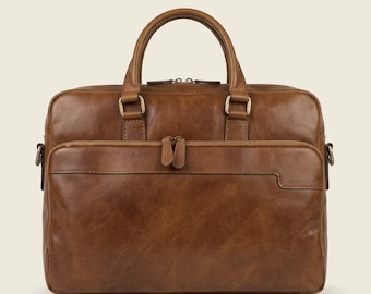 Peut inclure: Une mallette en cuir marron clair avec une silhouette rectangulaire, deux poignées supérieures et une grande poche frontale zippée. Le sac présente des ferrures en laiton vieilli, des doubles tirettes et des anneaux en D sur les côtés.