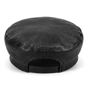A black leather fiddler newsboy cap featuring a textured, slightly distressed surface, a rounded crown, and a structured brim. The back of the cap includes an adjustable strap with a matching black buckle for a secure and customisable fit.