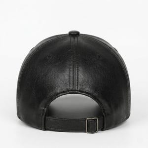 A black baseball cap with a textured finish, featuring a six-panel construction with a central button on top and a matching adjustable strap at the back secured with a rectangular metal buckle for a customisable fit.