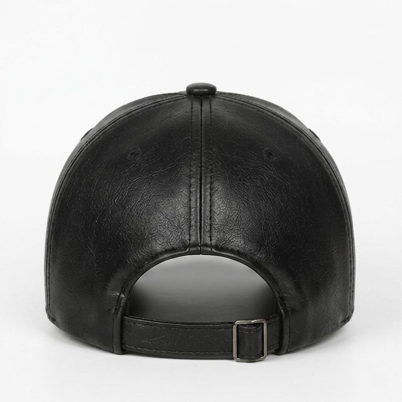 A black baseball cap with a textured finish, featuring a six-panel construction with a central button on top and a matching adjustable strap at the back secured with a rectangular metal buckle for a customisable fit.