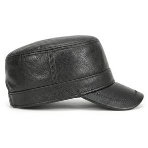 May include: A black military-style cap with a textured, leather-like finish. The hat features a flat, structured top, a wide band encircling the base, and a short, curved brim with visible stitching along the edge, presented in a side profile view.