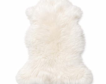 Peut inclure: Un tapis en peau de mouton blanc cassé, doté d'une texture épaisse, dense et à poils longs. Le tapis présente une forme organique et irrégulière qui imite la silhouette naturelle d'une peau, avec des fibres douces couvrant toute la surface.