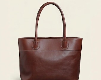Puede incluir: Un bolso tote de cuero marrón con dos asas. El bolso tiene forma rectangular con un diseño estructurado. Las asas están unidas al bolso con costuras reforzadas. El bolso está hecho de cuero liso y pulido.
