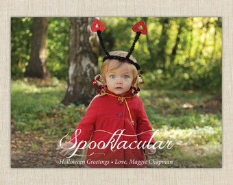 Könnte beinhalten: Eine rechteckige Grußkarte mit einem Kind in einem roten Mantel und einem schwarzen Haarreif mit herzförmigen Antennen. Der Text Spooktacular Halloween Greetings Love, Maggie Chapman steht in Weiß vor einem Waldhintergrund.