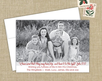 May include: A black and white photo of a family of five, including two parents and three children, sitting in a grassy area. The photo is framed with a white border and includes a red handwritten message that reads "I have come that they may have life, and have it to the full" John 10:10. The message also includes the family's last name and the names of each family member.
