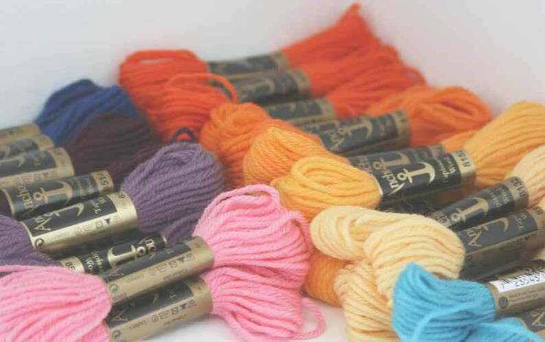Puede incluir: Surtido de carretes de hilo de bordar de la marca Anchor en varios colores, incluyendo morado, rosa, naranja, amarillo y azul. Cada carrete tiene una etiqueta dorada con el logotipo y el texto de Anchor.