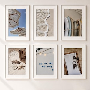 May include: A gallery wall of six framed prints featuring beach-themed photography. Images include white umbrellas against a blue sky, ocean foam on sand, surfboards, seashells with a basket, a wall with the text FROM THE SEA WITH LOVE, and a bikini.