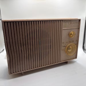 May include: A vintage Emerson radio in a brown and tan color scheme. The radio features a vertical grill design on the front and gold-colored knobs and dials. The word "EMERSON" is printed on the top right corner.