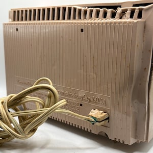 May include: A vintage, tan-colored radio with a cord. The radio has a ribbed design on the front and a vent on top. The text "Corporation Jersey City, N.J. USA" is visible on the back of the radio.