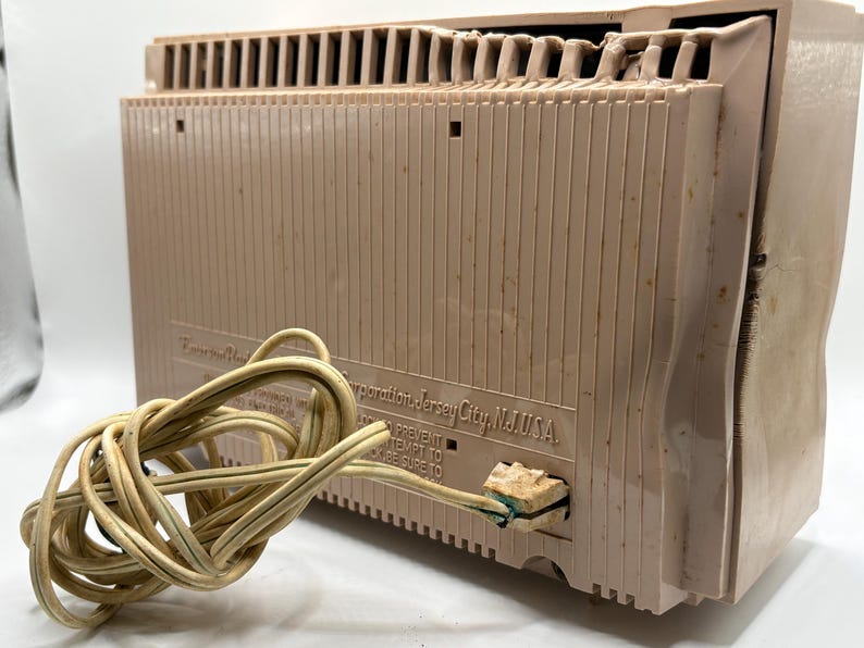 May include: A vintage, tan-colored radio with a cord. The radio has a ribbed design on the front and a vent on top. The text "Corporation Jersey City, N.J. USA" is visible on the back of the radio.