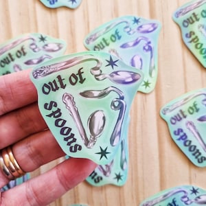 May include: A collection of stickers with a teal and purple color scheme. Each sticker features various spoon illustrations and the text "out of spoons". The stickers have a star design element.
