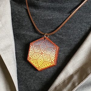 May include: A brown leather cord necklace with a hexagonal pendant. The pendant is made of wood and has a geometric design in shades of yellow, blue, and red.