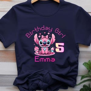 May include: Navy blue t-shirt featuring a pink cartoon character with the text "Birthday Girl" and the number "5". The character is holding cupcakes, and the name "Emma" is displayed below.