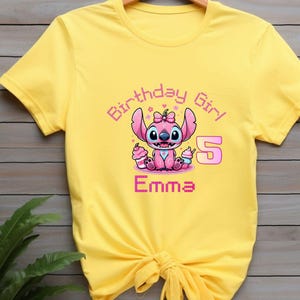 May include: Yellow t-shirt featuring a pink cartoon character with the text "Birthday Girl 5 Emma". The character is holding two cupcakes. The text and character are in pink and purple.