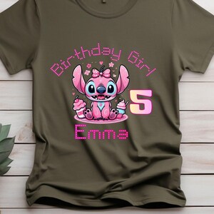 May include: Olive green t-shirt featuring a pink cartoon character with large ears, a bow, and the text "Birthday Girl!" and "5". The name "Emma" is also displayed in pink. The character is holding cupcakes.