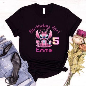 May include: Black t-shirt featuring a pink cartoon character with the text "Birthday Girl" and "Emma 5". The character is holding cupcakes. The design is in a cute, colorful style.