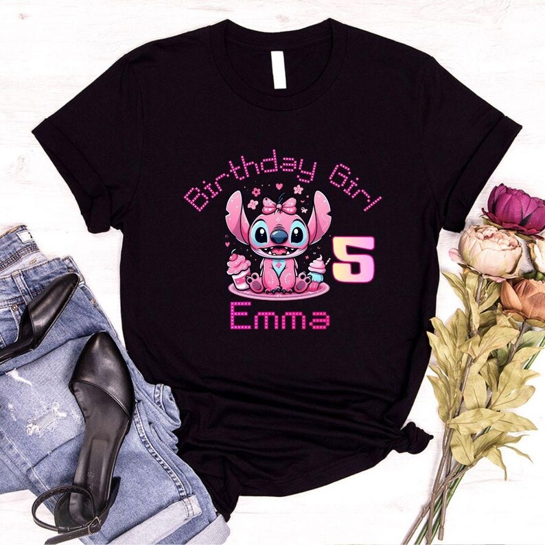 May include: Black t-shirt featuring a pink cartoon character with the text "Birthday Girl" and "Emma 5". The character is holding cupcakes. The design is in a cute, colorful style.