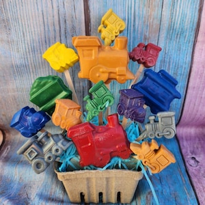 May include: A colorful arrangement of train-shaped crayons in a brown basket. The crayons are arranged in a rainbow pattern, with red, orange, yellow, green, blue, and purple crayons. The crayons are all in the shape of a train engine, with wheels and a smokestack.