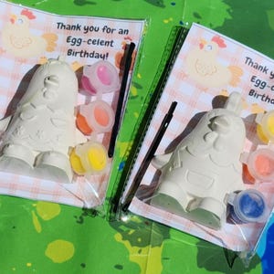 Puede incluir: Dos figuritas de pollo de cerámica blanca con botes de pintura y pinceles. Las figuritas están listas para ser pintadas. El embalaje incluye el texto "¡Gracias por un cumpleaños Egg-celente!"