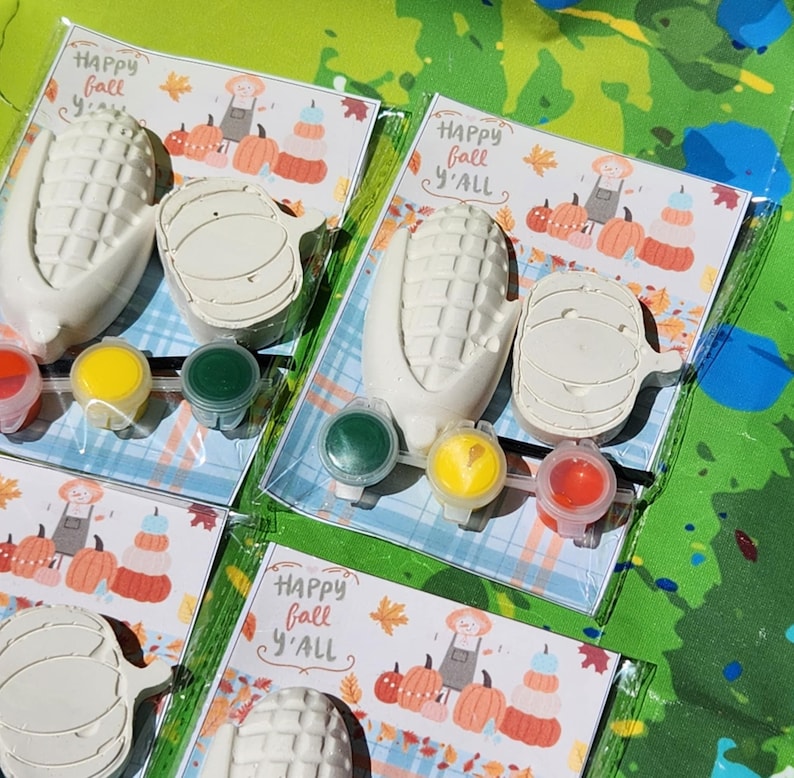 Peut inclure: Trois ensembles de kits de bricolage sur le th&egrave;me de l'automne &agrave; peindre soi-m&ecirc;me. Chaque kit comprend un &eacute;pi de ma&iuml;s, une citrouille et quatre petits pots de peinture. Les kits sont emball&eacute;s dans des sacs en plastique transparent avec une carte qui dit "Happy Fall Y'all".