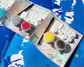 May include: A set of four paint-your-own cement trucks with paint pots and brushes. The trucks are white and the paint pots are red, yellow, blue, and brown. The packaging includes the text "Thank you for a tinkin' good time!"