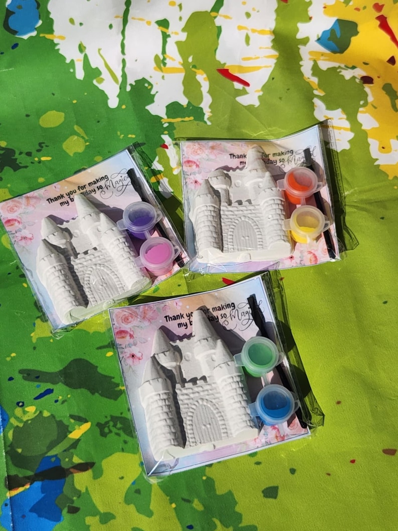 May include: Three castle-shaped paint kits in clear plastic packaging. Each kit includes a white castle, small paint pots in various colors, and a paintbrush. The packaging has text that reads "Thank you for making my birthday so Magic".