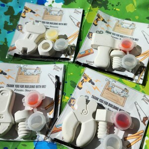 May include: Four favour bags with a white toy wrench and screw, a small container of paint, and a thank you note that reads "Thank you for building with me! From: Snazzy".