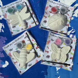 May include: Four paint-your-own insect kits. Each kit includes a white ceramic insect, paint pots in various colors, and a paintbrush. The kits are packaged in clear plastic bags with the text "Thank you for Creeping by!" printed on the card.
