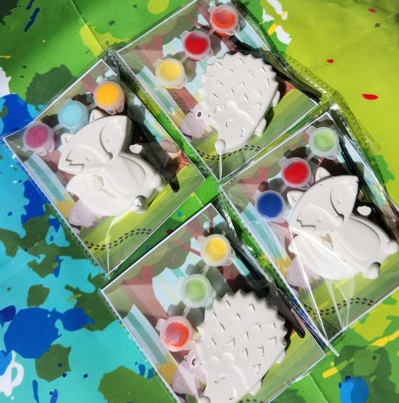 May include: Four paint-your-own ceramic animal kits. Each kit includes a ceramic animal, a paintbrush, and a set of paint pots. The animals are a fox, a hedgehog, and two hedgehogs. The paint pots are in various colors, including red, blue, green, yellow, and orange.