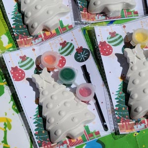 May include: A Christmas tree painting kit with a white ceramic tree, paint pots in red, green, orange, and yellow, a paintbrush, and a festive background.