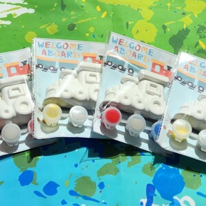 May include: Four white ceramic train engine figurines with the words "Welcome Aboard" on the front. Each figurine comes with four small pots of paint in different colors: red, yellow, white, and green.