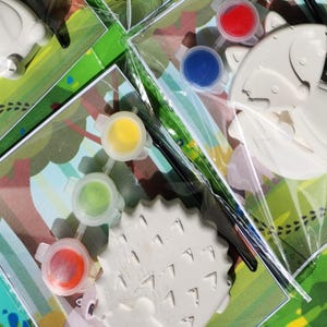 May include: A paint-your-own craft kit featuring three different animal shapes: a hedgehog, a butterfly, and a fox. The kit includes four small pots of paint in red, blue, yellow, and green.
